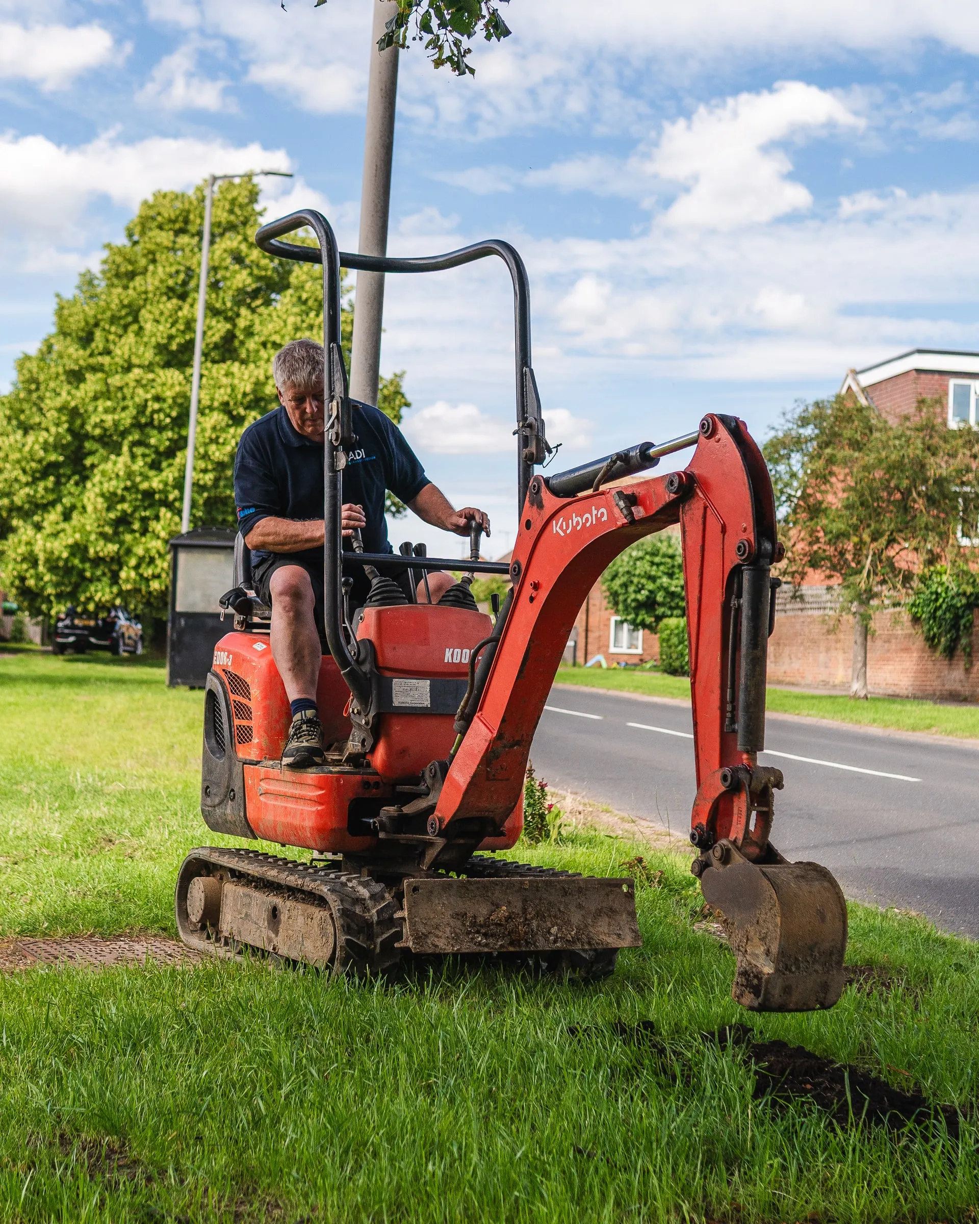 Engineer operating a mini digger to open the ground on a grass verge beside a road