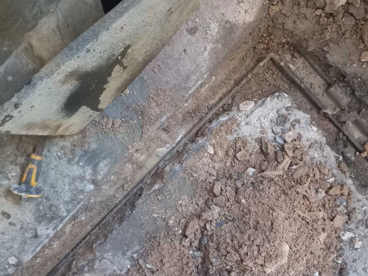 A channel opened in a Coventry hallway floor, exposing pipework beside lifted flooring and a hammer